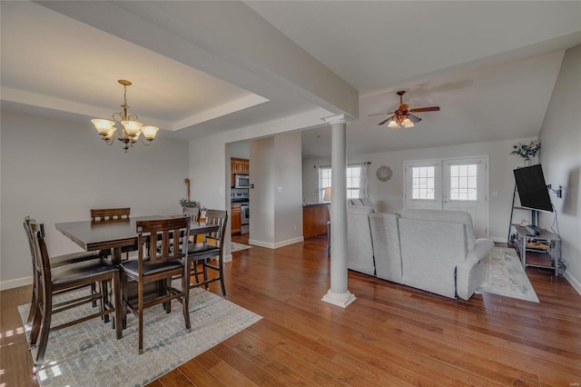 dining area with decorative columns, light hardwood / wood-style floors, a tray ceiling, and ceiling fan with notable chandelier