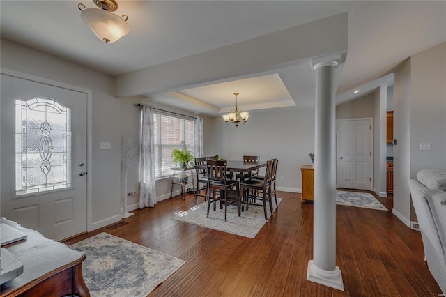 dining area with a tray ceiling, dark hardwood / wood-style flooring, ornate columns, and an inviting chandelier