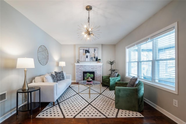 living room with hardwood / wood-style flooring, plenty of natural light, an inviting chandelier, and a brick fireplace