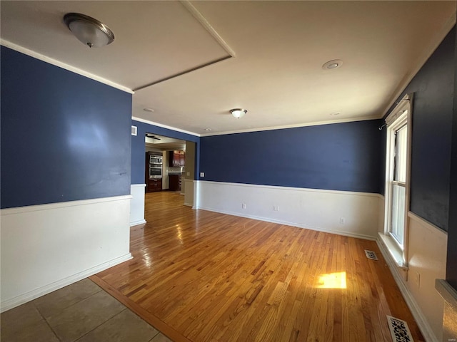 spare room featuring visible vents, wood finished floors, crown molding, and wainscoting