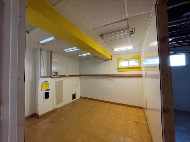 basement with light parquet floors and a paneled ceiling