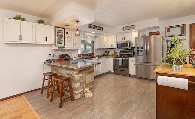 kitchen featuring a breakfast bar area, appliances with stainless steel finishes, hanging light fixtures, white cabinets, and kitchen peninsula