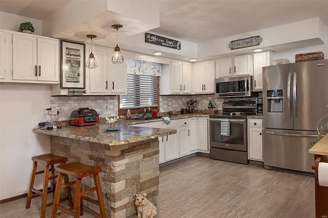 kitchen featuring appliances with stainless steel finishes, pendant lighting, white cabinetry, dark stone counters, and kitchen peninsula