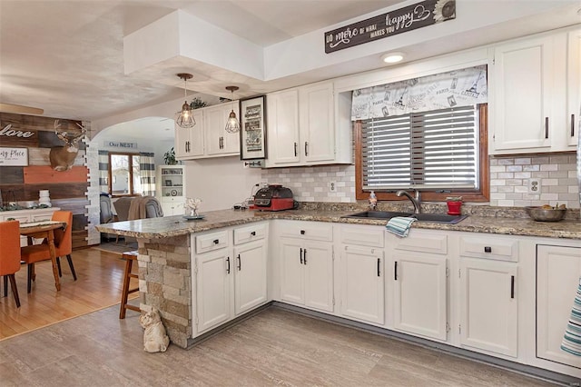 kitchen featuring sink, white cabinetry, hanging light fixtures, light wood-type flooring, and kitchen peninsula