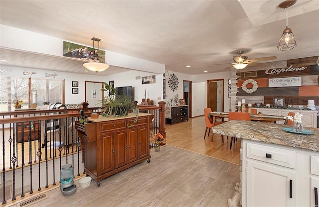 kitchen featuring light stone countertops, pendant lighting, white cabinets, and light hardwood / wood-style flooring