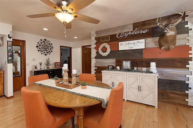 dining room with ceiling fan, wooden walls, and light hardwood / wood-style flooring