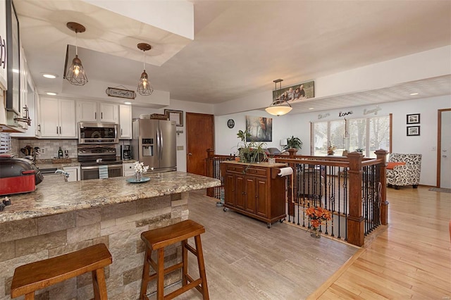 kitchen with white cabinetry, stainless steel appliances, decorative light fixtures, kitchen peninsula, and light wood-type flooring