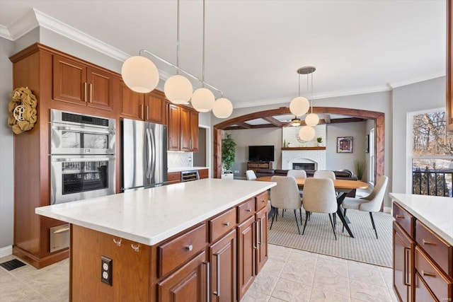 kitchen featuring pendant lighting, appliances with stainless steel finishes, a center island, a fireplace, and ornamental molding