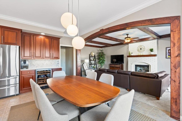 dining area with a brick fireplace, crown molding, beverage cooler, and beamed ceiling