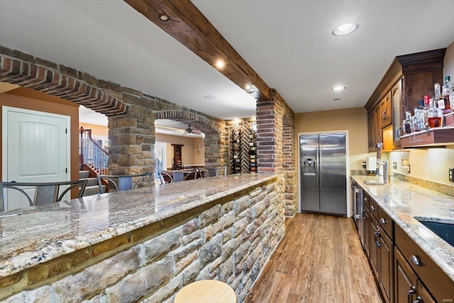 kitchen featuring light stone counters, stainless steel fridge, decorative columns, and light hardwood / wood-style flooring