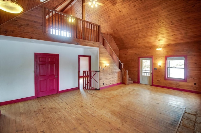 unfurnished living room with wood-type flooring, wooden walls, and high vaulted ceiling