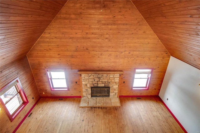 unfurnished living room featuring wood ceiling, plenty of natural light, light hardwood / wood-style flooring, and a stone fireplace