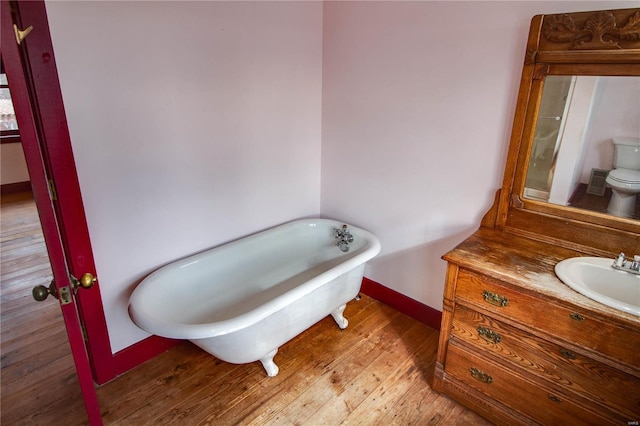 bathroom featuring wood-type flooring, toilet, vanity, and a tub to relax in