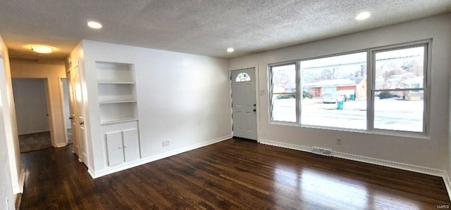 spare room featuring built in shelves, dark hardwood / wood-style floors, and a textured ceiling