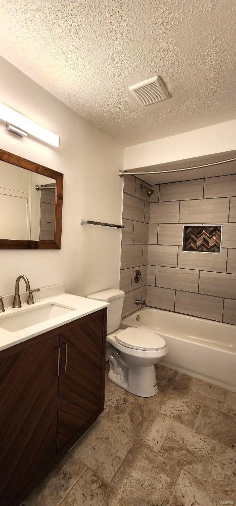 full bathroom with vanity, toilet, a textured ceiling, and tiled shower / bath combo