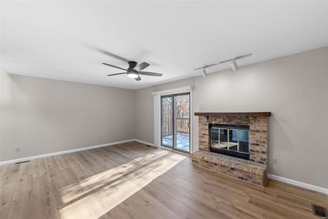 unfurnished living room with a fireplace, rail lighting, ceiling fan, and light wood-type flooring