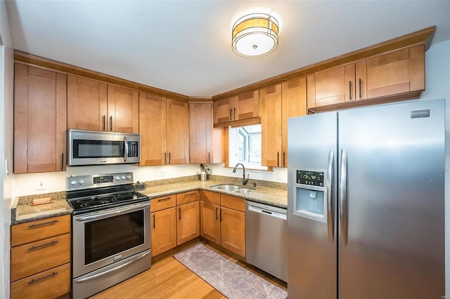 kitchen with light stone counters, appliances with stainless steel finishes, sink, and light wood-type flooring