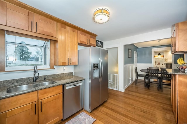 kitchen featuring sink, light hardwood / wood-style flooring, dark stone countertops, appliances with stainless steel finishes, and pendant lighting