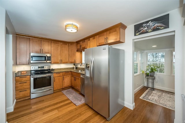 kitchen with stainless steel appliances, sink, dark stone countertops, and light wood-type flooring