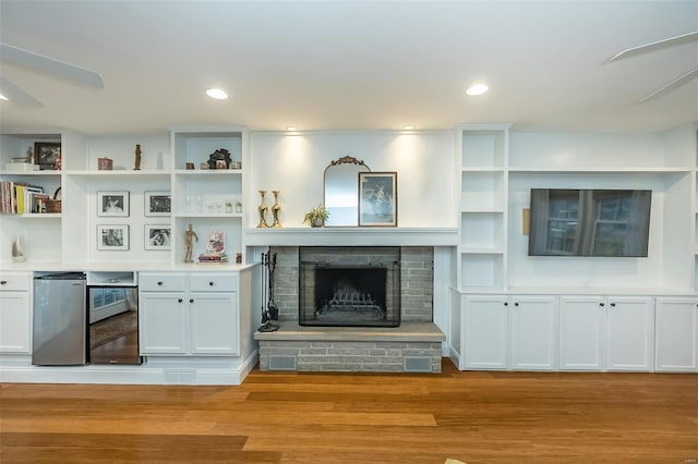 unfurnished living room with ceiling fan, a brick fireplace, and light wood-type flooring