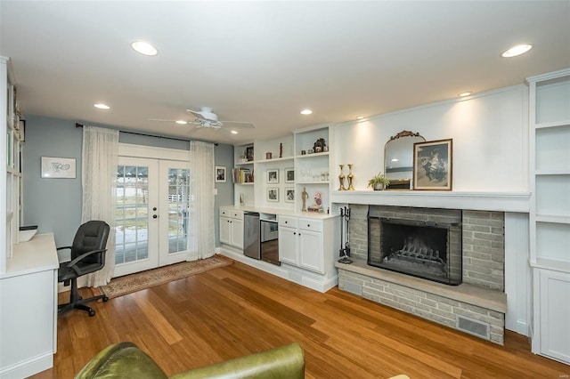 living room with french doors, built in features, ceiling fan, a fireplace, and light hardwood / wood-style floors