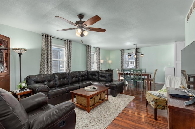 living room with ceiling fan with notable chandelier, dark wood-type flooring, and a textured ceiling