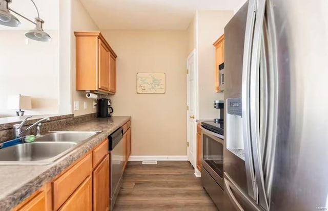 kitchen featuring appliances with stainless steel finishes, sink, dark wood-type flooring, and decorative light fixtures