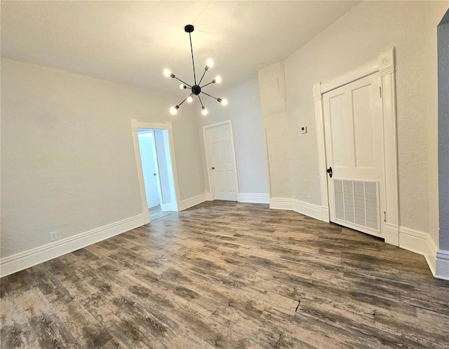 spare room with an inviting chandelier and dark hardwood / wood-style flooring