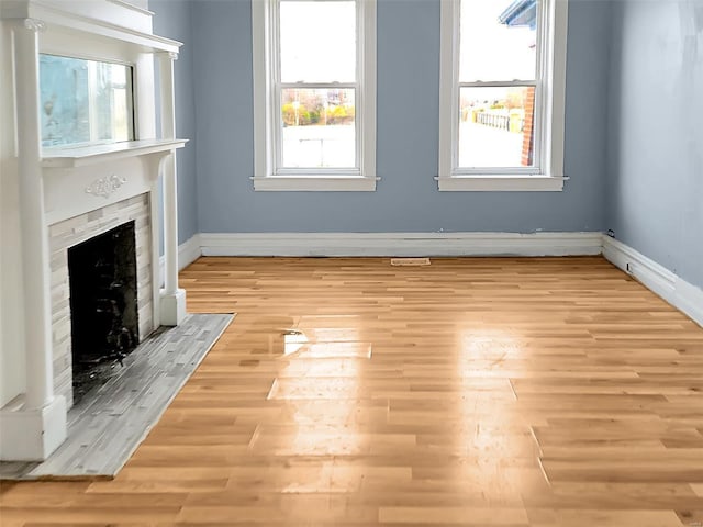 unfurnished living room with a tiled fireplace and light wood-type flooring