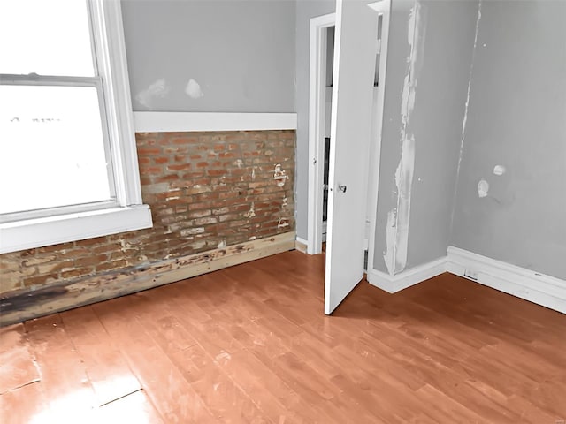 spare room with brick wall and light hardwood / wood-style flooring