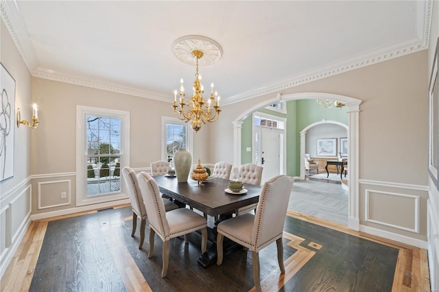 dining room with crown molding, a notable chandelier, wood-type flooring, and ornate columns