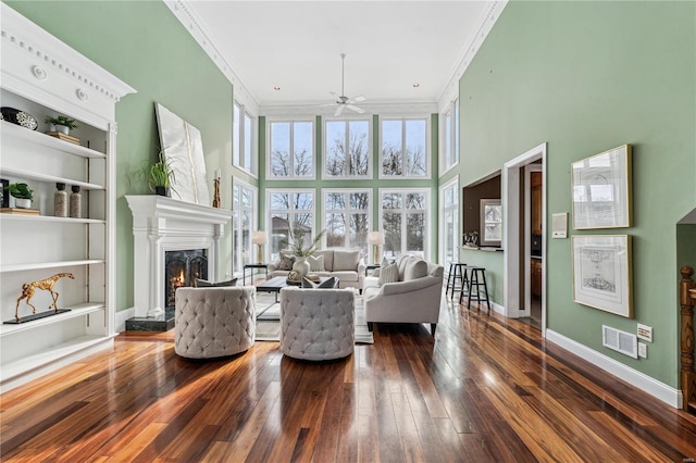 living room with built in features, a fireplace, dark hardwood / wood-style flooring, a high ceiling, and ornamental molding