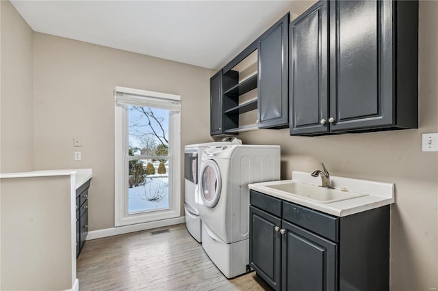 clothes washing area featuring cabinets, sink, light hardwood / wood-style floors, and washing machine and clothes dryer