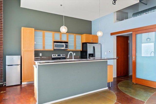 kitchen featuring light brown cabinetry, appliances with stainless steel finishes, pendant lighting, a kitchen island with sink, and a high ceiling