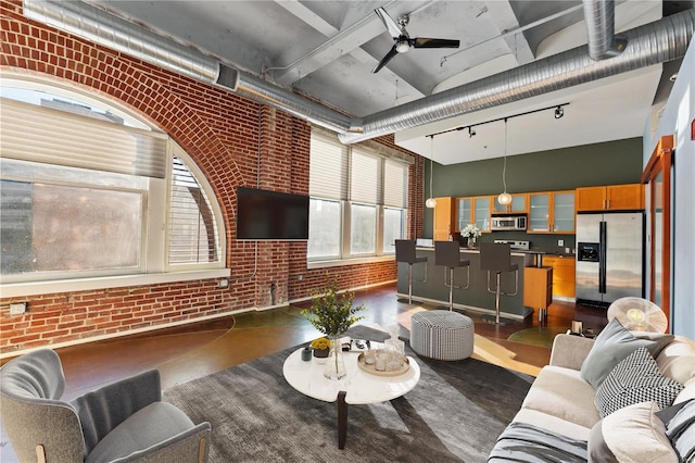 living room with a high ceiling, rail lighting, brick wall, and ceiling fan