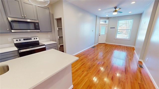 kitchen featuring ceiling fan, appliances with stainless steel finishes, gray cabinets, and light hardwood / wood-style flooring