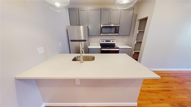 kitchen with sink, appliances with stainless steel finishes, a kitchen breakfast bar, gray cabinets, and kitchen peninsula