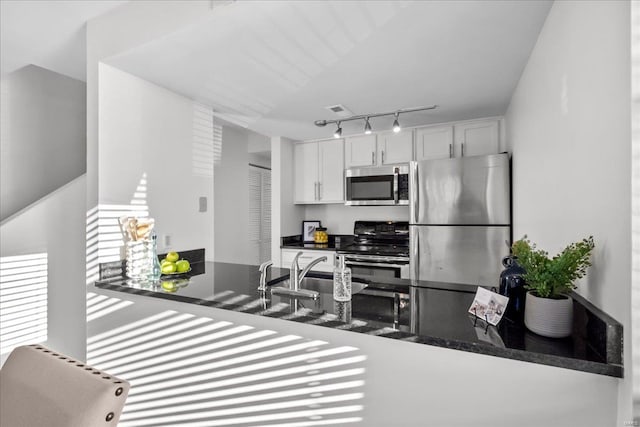 kitchen featuring sink, white cabinetry, appliances with stainless steel finishes, kitchen peninsula, and dark stone counters