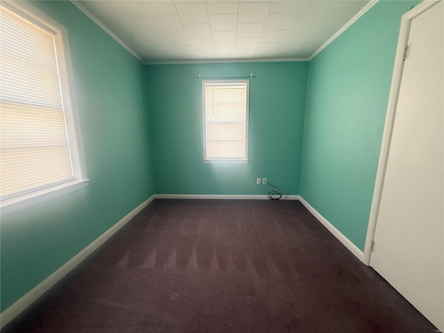 unfurnished room featuring a wealth of natural light, ornamental molding, and dark colored carpet