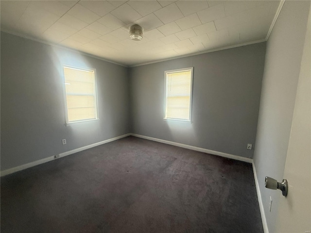 empty room featuring crown molding, dark colored carpet, and a healthy amount of sunlight