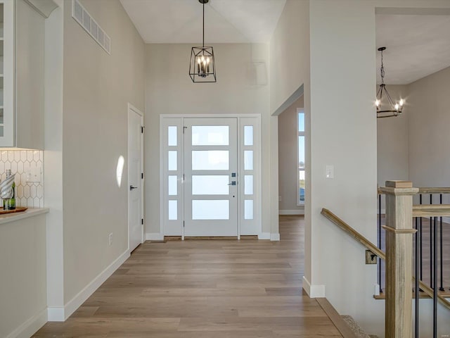 entryway with a towering ceiling, light hardwood / wood-style floors, and a notable chandelier