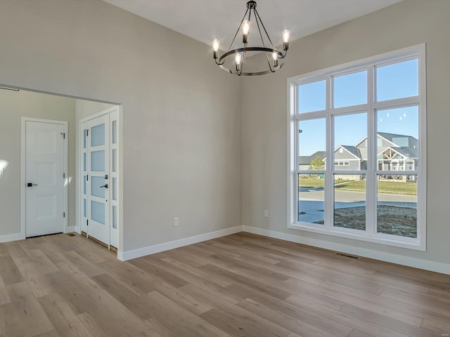 empty room with light hardwood / wood-style flooring and a chandelier