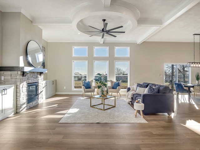 living room featuring a stone fireplace, ceiling fan with notable chandelier, wood-type flooring, coffered ceiling, and beam ceiling