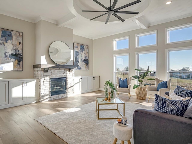 living room with beam ceiling, ceiling fan, a stone fireplace, and light hardwood / wood-style floors