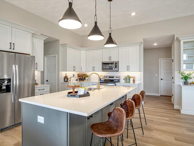 kitchen featuring hanging light fixtures, stainless steel appliances, an island with sink, and white cabinets