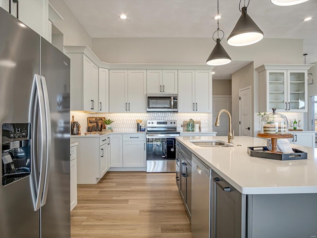 kitchen featuring appliances with stainless steel finishes, decorative light fixtures, white cabinetry, sink, and a center island with sink