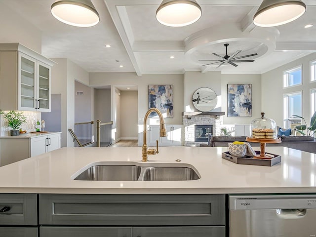 kitchen featuring sink, gray cabinets, dishwasher, an island with sink, and a stone fireplace