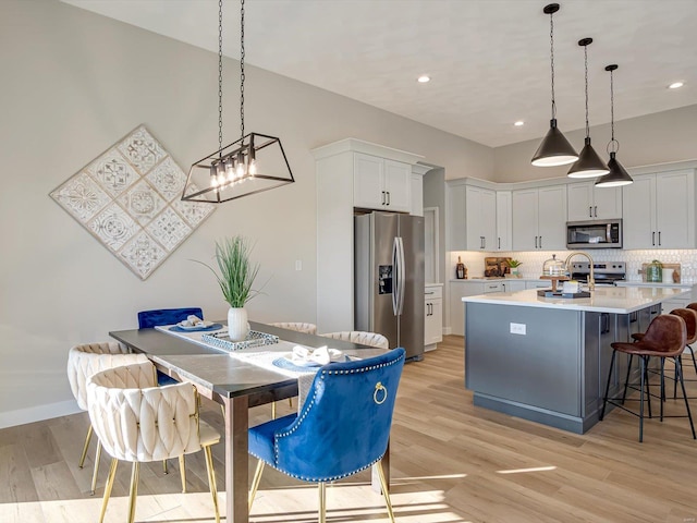 kitchen with white cabinetry, an island with sink, hanging light fixtures, stainless steel appliances, and light wood-type flooring