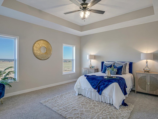 carpeted bedroom with ceiling fan and a raised ceiling