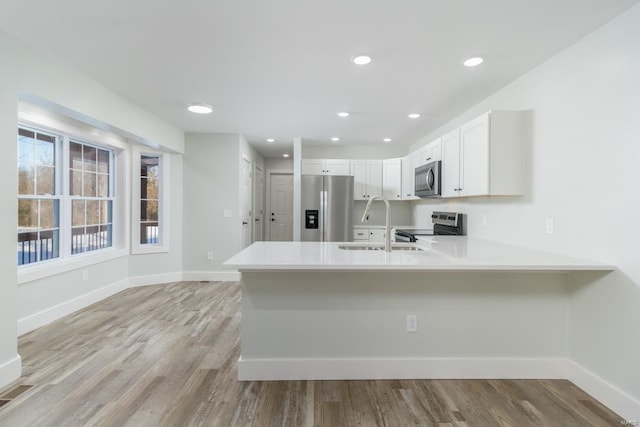 kitchen with appliances with stainless steel finishes, white cabinets, sink, light hardwood / wood-style flooring, and kitchen peninsula